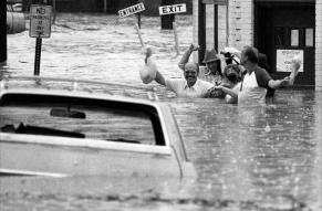 Black and white photograph of a group of men wading through heavily flooded streets.