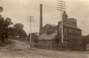 Black and white photograph of a railway track and road alongside a grain-milling factory.