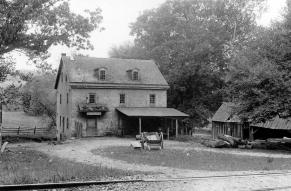 Black and white image of a ca. 1900 rural post office building fronted by railroad tracks.