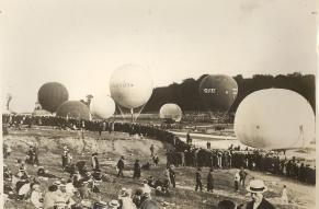 Black and white image showing a crowd assembled at the start of a hot air balloon race. A number of grounded balloons are in the image.