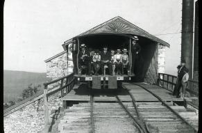 Black and white image of passengers in an open-backed train car.