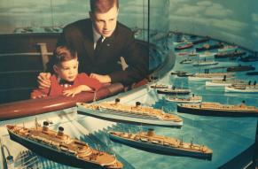 Color photograph of a man and child looking at an exhibit of model ships.