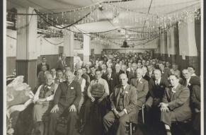 Black and white image of a large number of seated people in a room with Christmas decorations