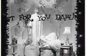 Black and white photograph of a Christmas themed store window display with the phrase 'Just for you darling' painted on the window.