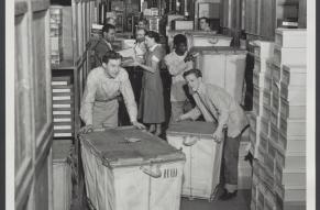 People working in a corridor of a storage room or warehouse of a Strawbridge & Clothier store.