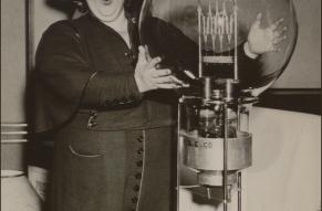 Black and white photo of a woman placing her hands on a very large incandescent light bulb.