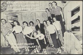 Postcard with black and white photograph of a group posed inside the Haunted Shack at Knott's Berry Farm 