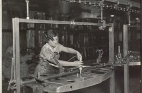 Black and white photograph of a woman in overalls applying fasteners to a metal door panel.