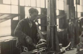 Black and white photograph of a worker in a factory riveting autobody parts.