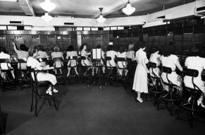 Black and white photo of a number of women at work in a large switchboard office.