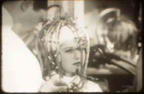 Gif of a woman recieving a beauty treatment that involves a cage over her head.