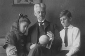 Black and white image of two children on either side of a man holding a striped sphere.