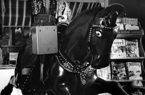 Black and white photograph of a child dressed like a cowboy on a coin-operated horse ride.