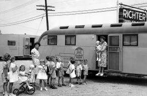 Black and white photograph of children lined up outside a trailer with a traveling museum exhbiit.