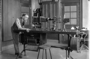 Black and white image of a young man looking into the end of equipment assembled on a tabletop.