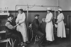 Black and white photograph of nurses and patients in machine shop dispensary.