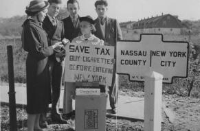 People buying and selling cigarettes by a sign demarcating the Nassau and New York City county line