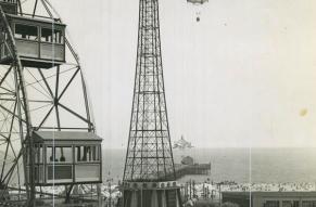 Black and white photograph, taken from a height, of a seaside amusement park. Main feature is the Parachute Jump ride.