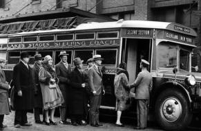 A black and white photograph of a group of people boarding a bus.