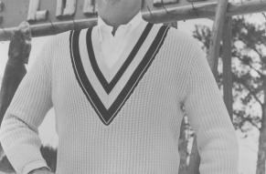 The image features a man wearing a sweater and standing outdoors. The photo is in black and white.