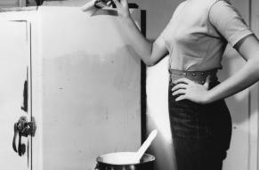 Black and white image of a woman painting a refrigerator