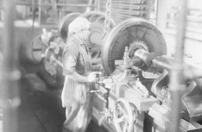Black and white image of a woman in a machine shop, working at a large lathe machine.