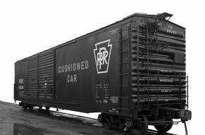 Black and white, 3/4 view of a railroad box car. Stenciling on side reads "Cushioned car".