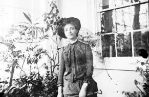 Black and white image of a woman holding a shovel in a greenhouse conservatory