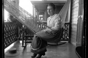 Black and white photograph of a woman in a hammock on a porch