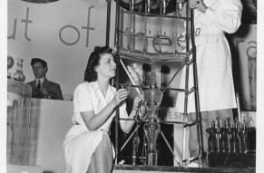 BBlack and white image of a man and woman at an exhibition showcasing a complex apparatus.