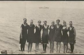 Black and white photograph of a group of women posed by the shore of a beach in 1916